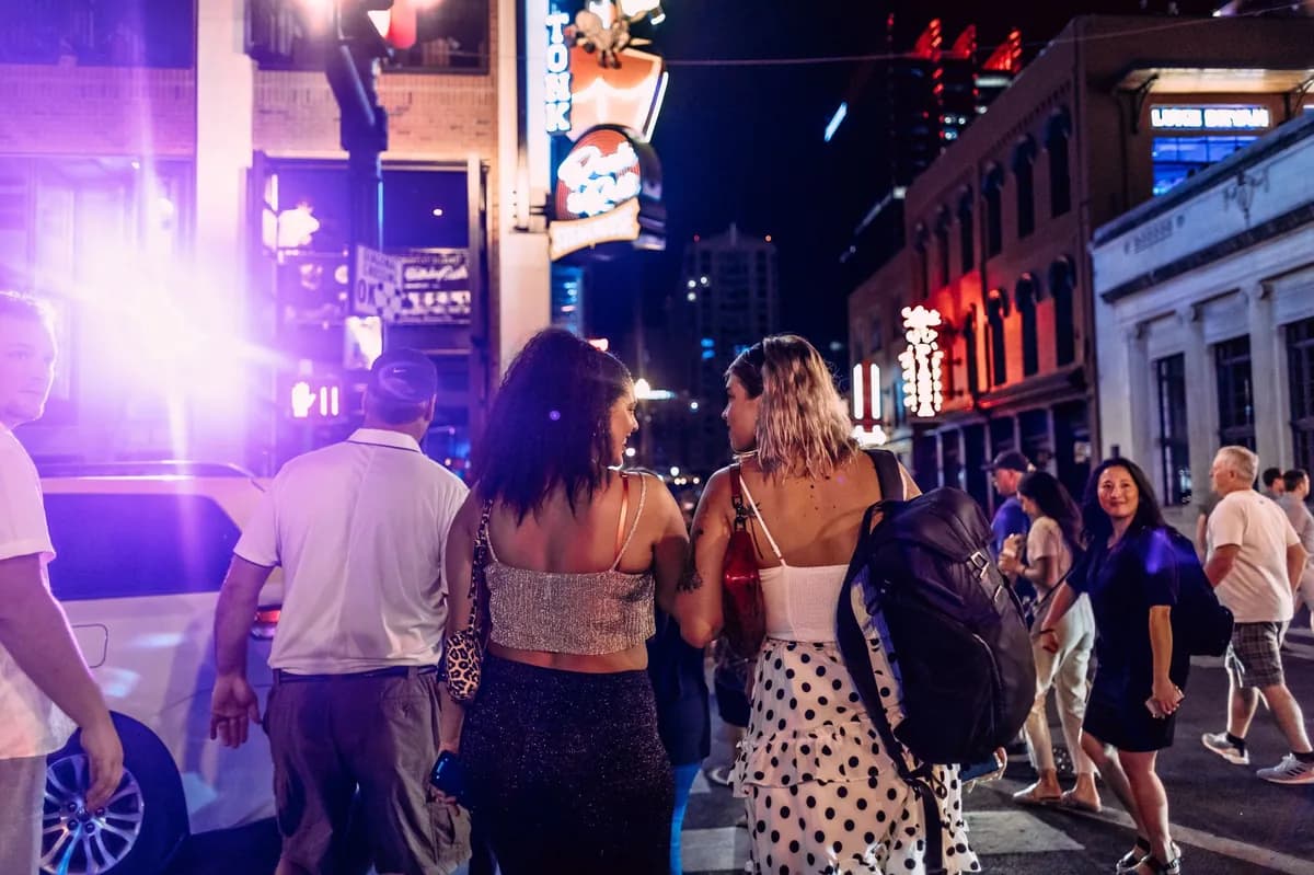 A group walking together down a neon-lit downtown bar strip at night — keeping the group together on a bar crawl