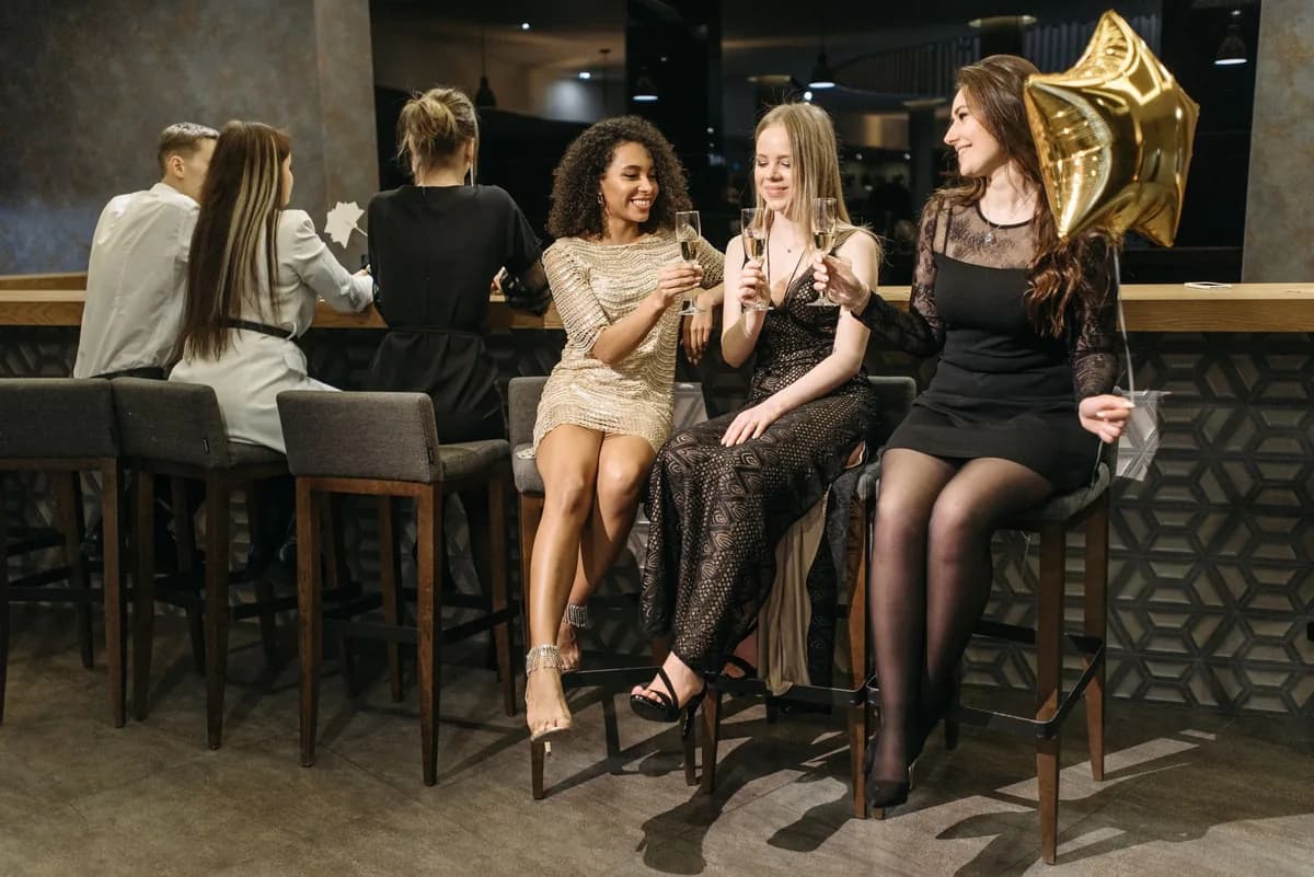 Three women in party dresses toasting champagne at a stylish bar with a gold star balloon on a night out