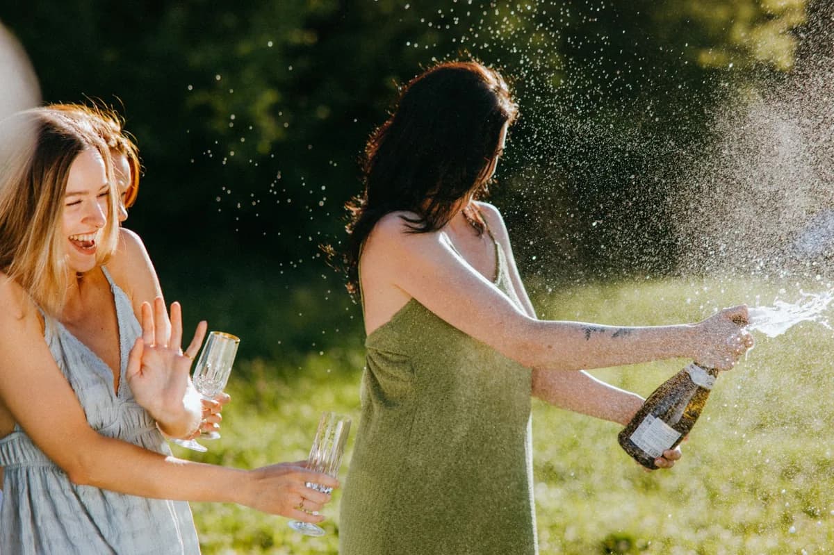 Two women celebrating outdoors as one pops a champagne bottle — a BYOB bachelorette celebration
