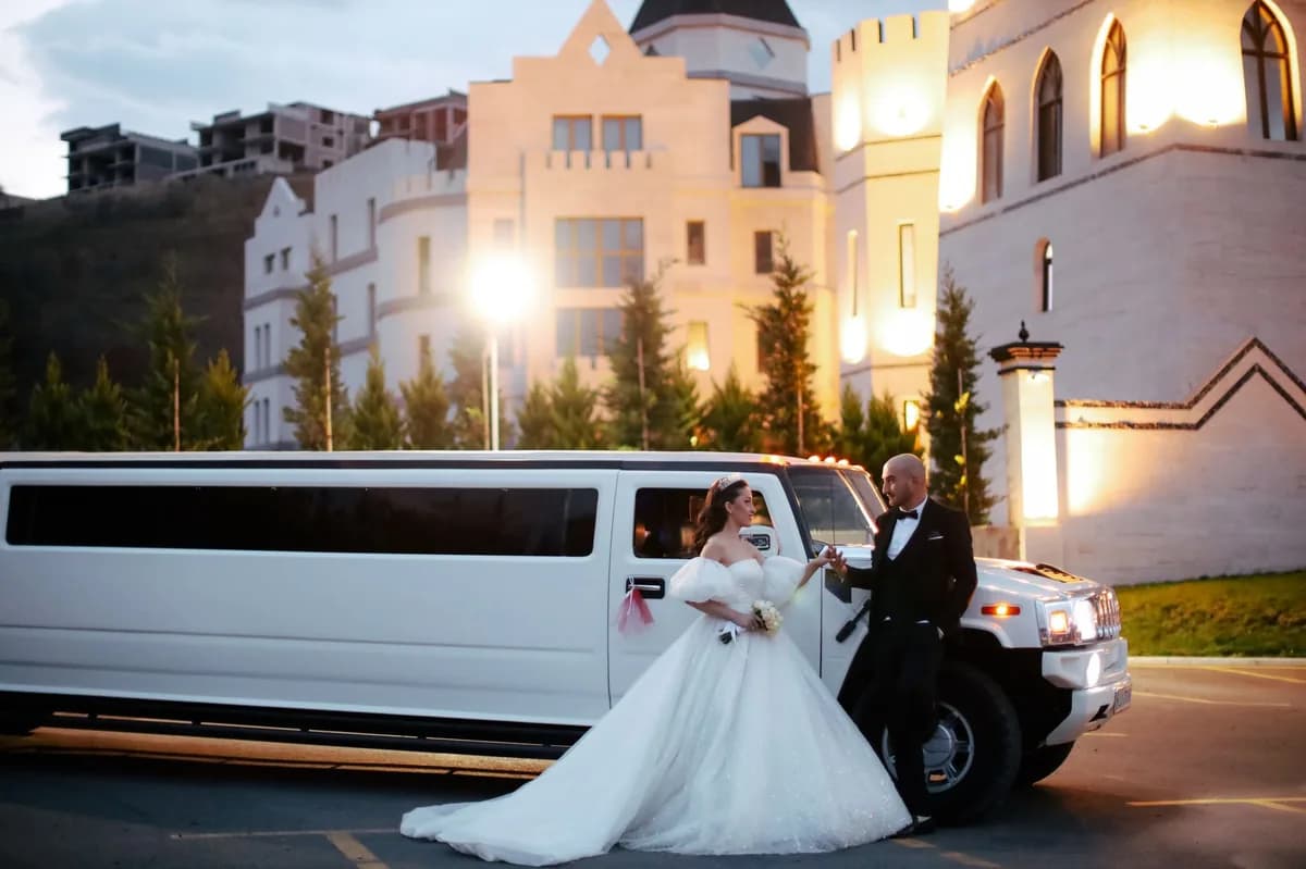 Bride and groom in formal attire beside a white stretch limousine outside an illuminated Chicago wedding venue