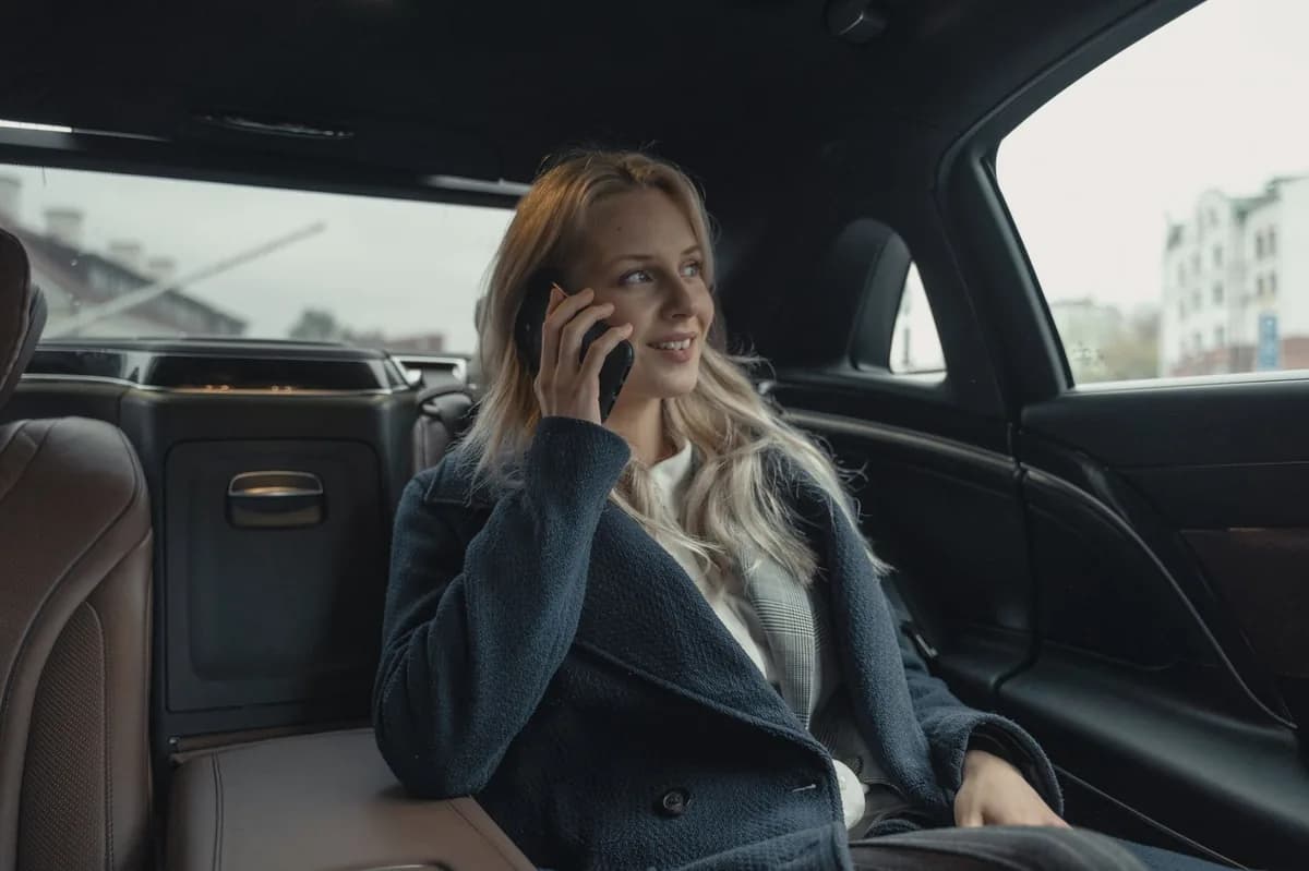 A businesswoman on her phone in the back seat of a luxury corporate car-service vehicle