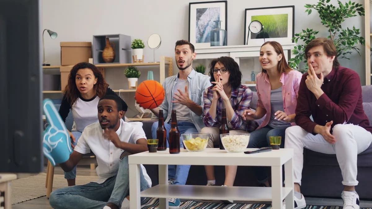 A group of sports fans cheering together with a foam finger and drinks — a game-day group ready to ride to the stadium