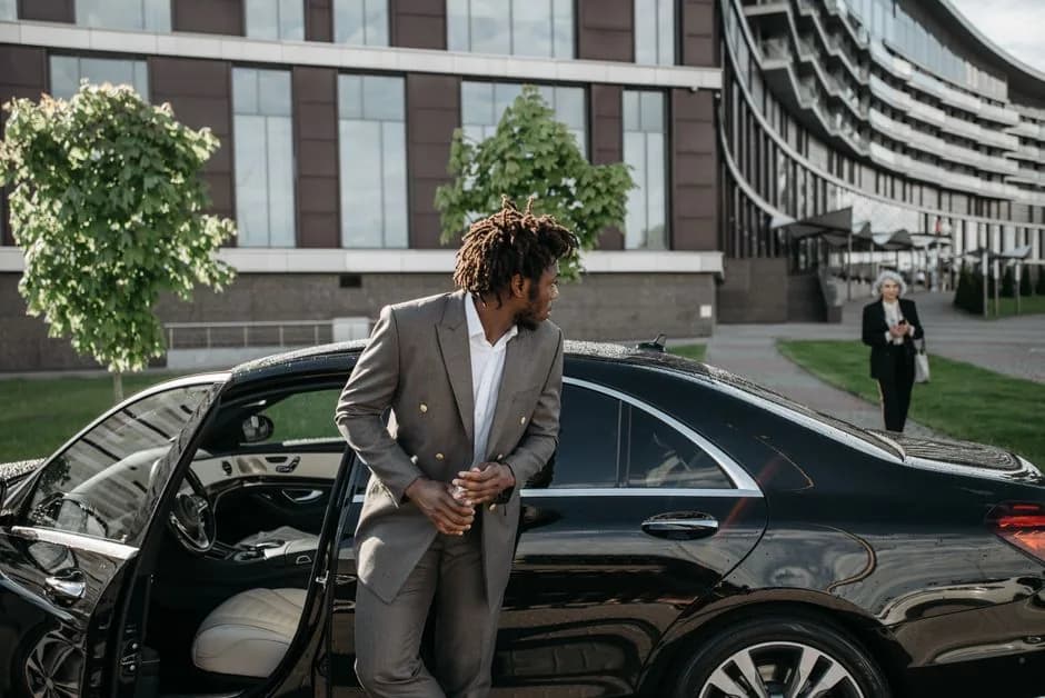 An executive in a suit stepping out of a black luxury car outside a modern office building for a meeting