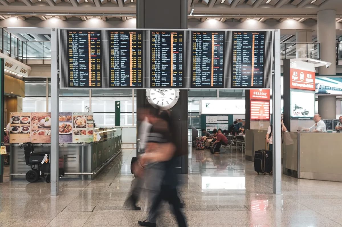 Traveler hurrying through an airport terminal past a large flight departure board with a wall clock overhead — timing your Chicago airport car pickup
