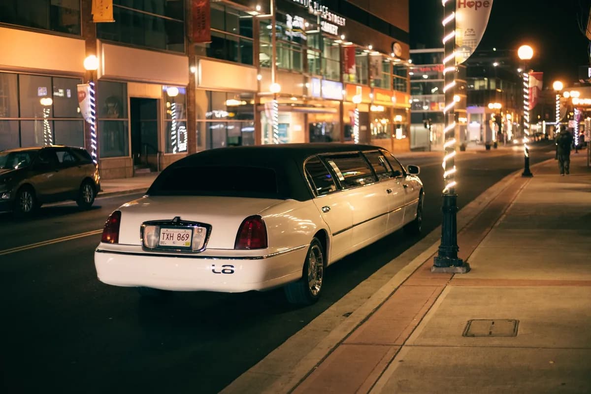 A white stretch limousine on a city street at night surrounded by glowing streetlights — booking prom transportation in advance