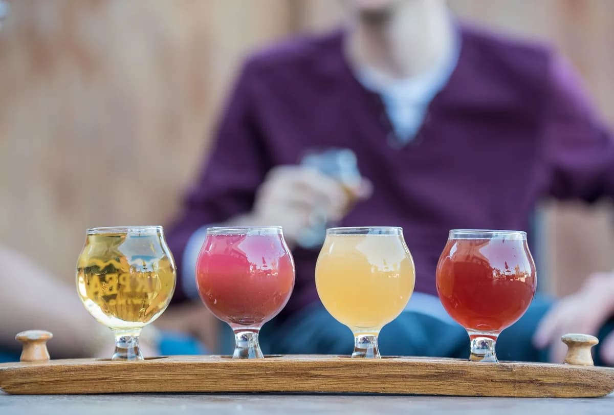 A colorful craft-beer tasting flight — four glasses on a wooden brewery paddle during a brewery tour