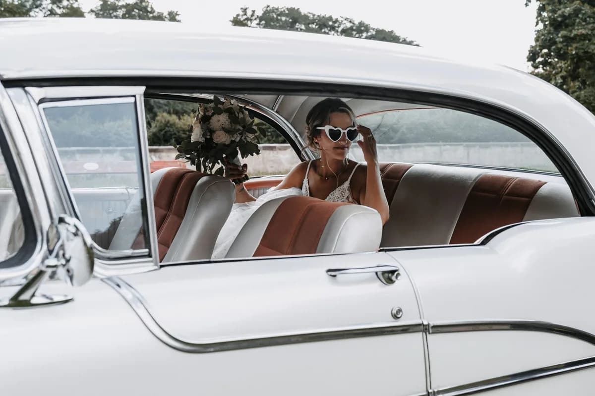 Bride with her bouquet seated inside a classic white vintage car — a wedding-vehicle option alongside limos and party buses
