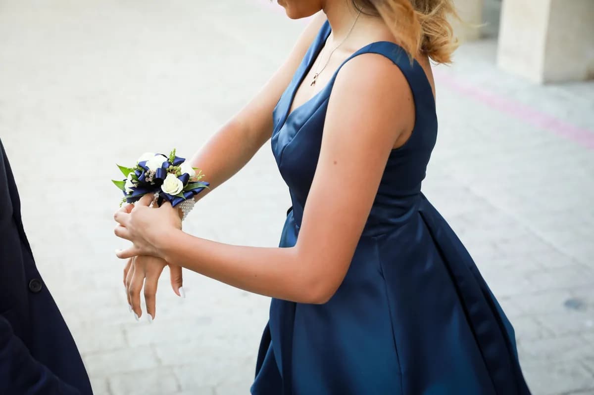 A young woman in a navy prom dress with a wrist corsage beside her date — a safe, chaperoned prom-night arrival