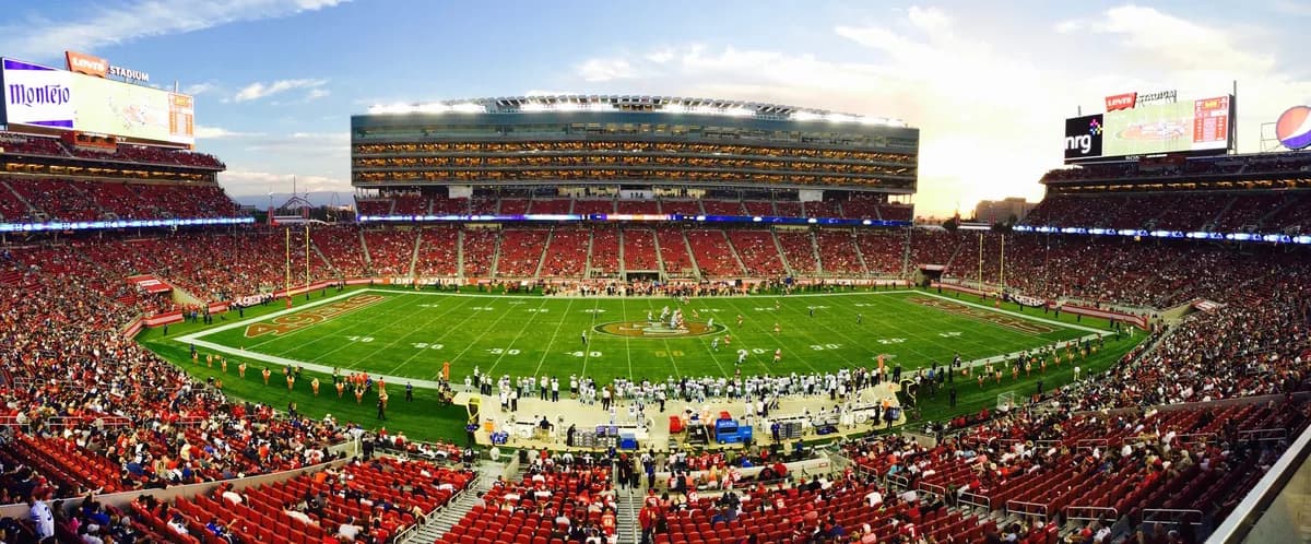 A sweeping panorama of a packed football stadium at sunset, every seat filled for game day