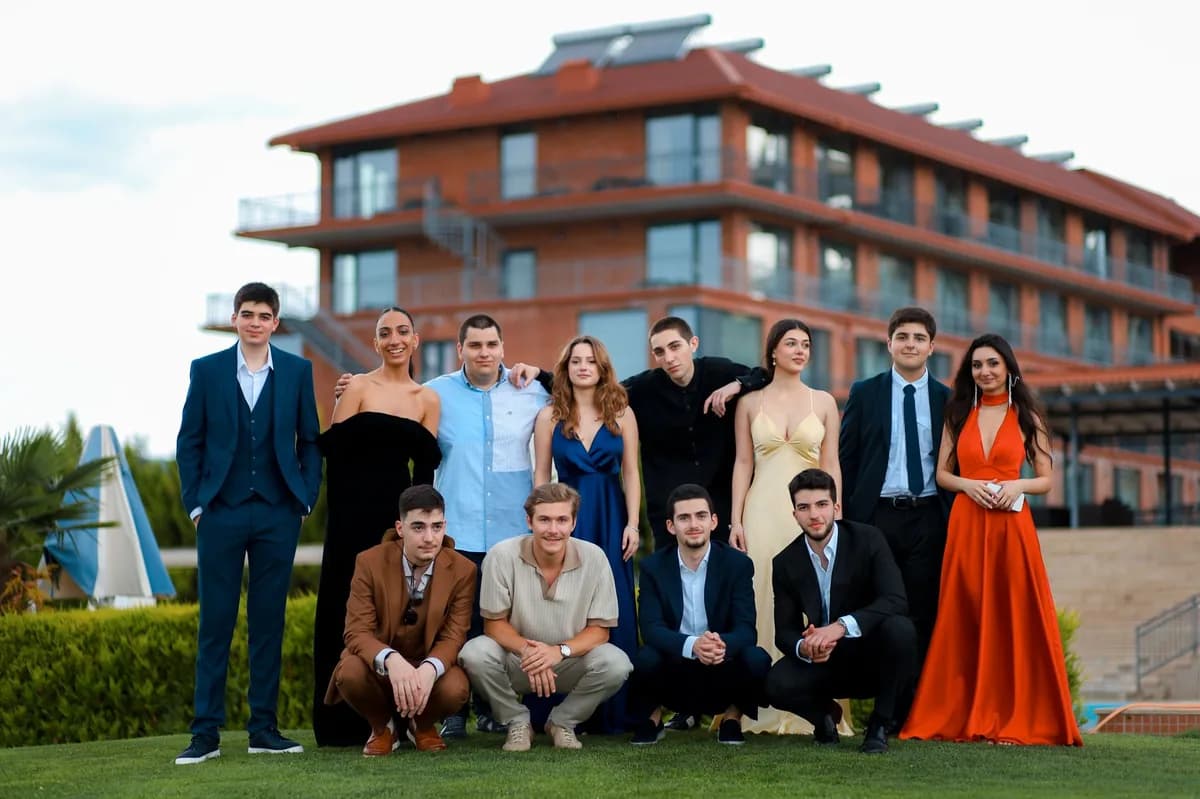 A large group of young adults in evening gowns and suits posing together outside a venue — splitting prom party-bus cost across the group