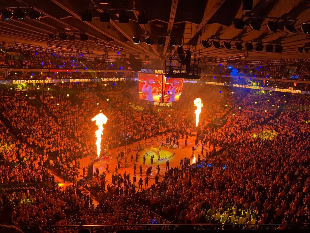 A massive indoor arena packed with fans during a basketball game, with pyrotechnics lighting the court at player introductions